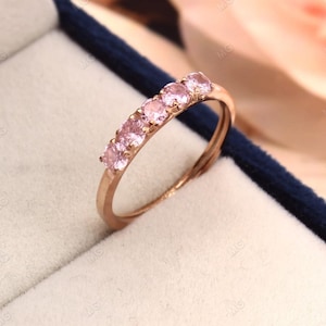 Puede incluir: Un anillo de banda de oro rosa con cinco piedras preciosas rosas engastadas en una fila.