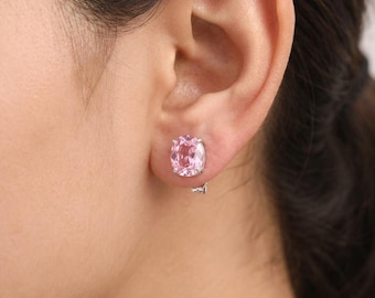 May include: A single oval-cut pink gemstone earring set in a silver-toned metal prong setting. The faceted stone displays a light pink hue and is secured by four prongs, attached to a small silver-toned metal backing visible on the earlobe.
