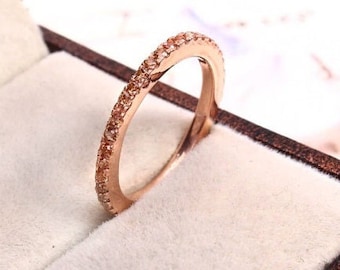 May include: A rose gold band ring with a row of small, clear stones set in the band.