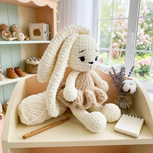 May include: A handmade, cream-colored crochet bunny doll with long floppy ears and a tan dress. A ball of cream yarn and a wooden crochet hook sit nearby. The bunny is a soft toy, perfect for a child's room or nursery.
