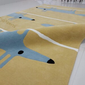 May include: A yellow rug with a repeating pattern of blue stylized foxes and white stripes. The rug is folded in half, showing the underside of the rug.