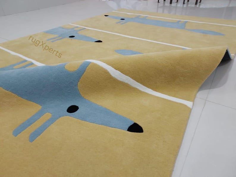 May include: A yellow rug with a repeating pattern of blue stylized foxes and white stripes. The rug is folded in half, showing the underside of the rug.