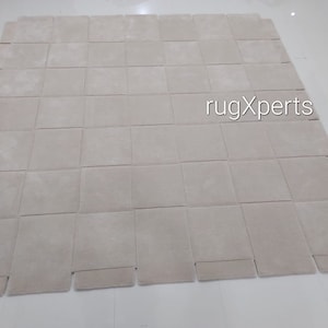 Pu&ograve; includere: Un grande tappeto di colore bianco sporco composto da quadrati singoli. Il tappeto &egrave; composto da 9 file di 9 quadrati, per un totale di 81 quadrati. Il tappeto &egrave; steso su un pavimento bianco. Il testo "rugXperts" &egrave; stampato al centro del tappeto.