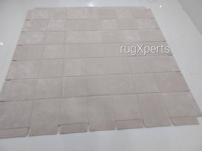 Pu&ograve; includere: Un grande tappeto di colore bianco sporco composto da quadrati singoli. Il tappeto &egrave; composto da 9 file di 9 quadrati, per un totale di 81 quadrati. Il tappeto &egrave; steso su un pavimento bianco. Il testo "rugXperts" &egrave; stampato al centro del tappeto.