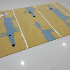 May include: A yellow rug with a blue and white fox design. The rug has a modern, minimalist style.