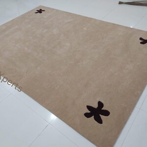 May include: A rectangular beige rug with four dark brown floral designs, one in each corner. The rug is made of a soft, plush material and is suitable for a living room or bedroom.