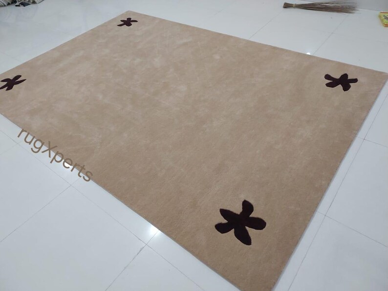 May include: A rectangular beige rug with four dark brown floral designs, one in each corner. The rug is made of a soft, plush material and is suitable for a living room or bedroom.