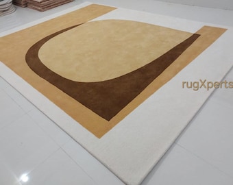 Puede incluir: Una alfombra blanca con un diseño geométrico marrón y beige. La alfombra tiene una forma curva en el centro y una forma cuadrada alrededor del borde. La alfombra está hecha de un material suave y mullido. rugXperts