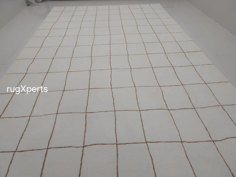 May include: White rug with a grid pattern of brown lines. The rug is made of a soft, plush material and has a subtle sheen.