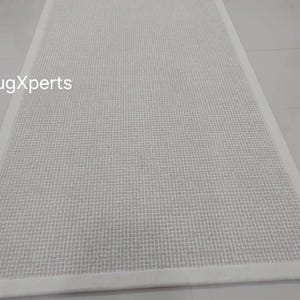May include: White woven rug with a white border. The rug has a subtle texture and is perfect for adding a touch of elegance to any room.