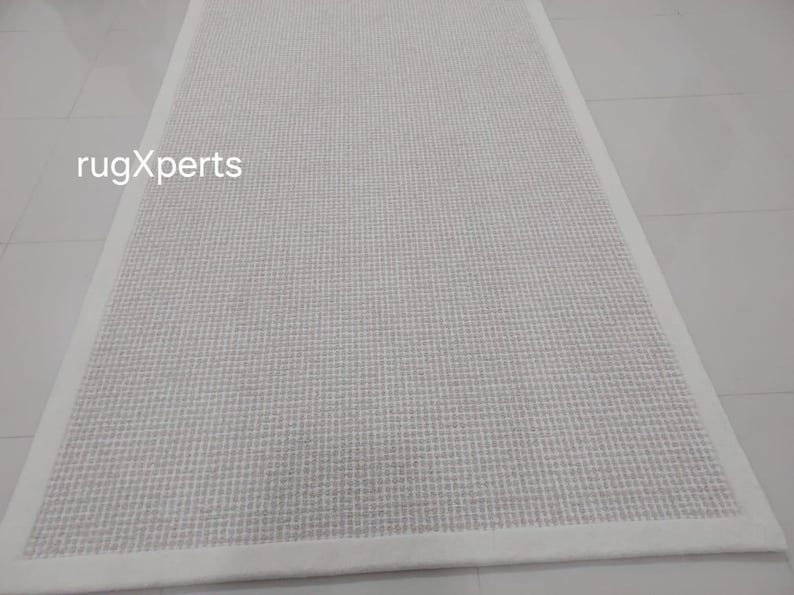 May include: White woven rug with a white border. The rug has a subtle texture and is perfect for adding a touch of elegance to any room.