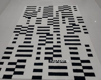 Può includere: Tappeto geometrico a motivi bianco e nero con un design moderno. Il tappeto ha uno sfondo bianco con strisce e quadrati neri.