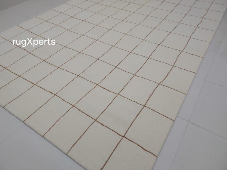 May include: White rug with a grid pattern of brown lines. The rug is made of wool and has a soft, luxurious feel.