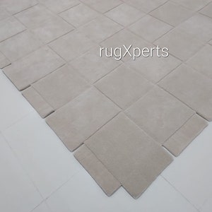 Pu&ograve; includere: Primo piano di un tappeto beige chiaro con un motivo intrecciato. Il tappeto &egrave; realizzato in un materiale morbido e soffice e ha una texture sottile. Il tappeto &egrave; steso su una superficie bianca.