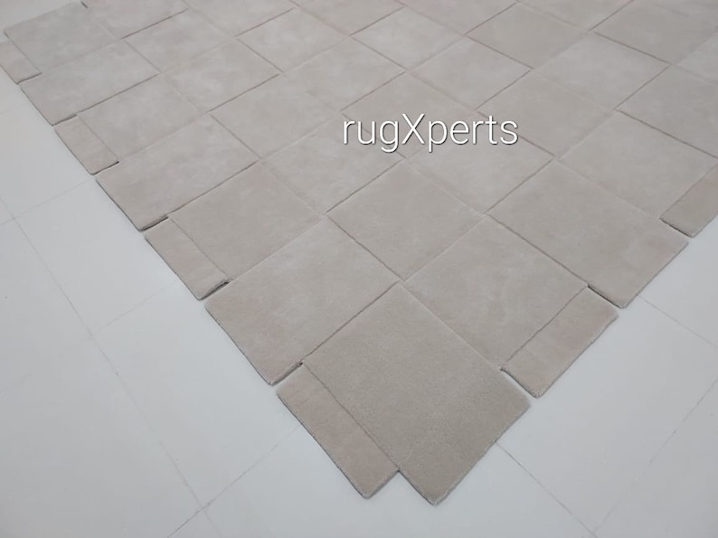 Pu&ograve; includere: Primo piano di un tappeto beige chiaro con un motivo intrecciato. Il tappeto &egrave; realizzato in un materiale morbido e soffice e ha una texture sottile. Il tappeto &egrave; steso su una superficie bianca.