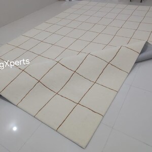 May include: A white rug with a grid pattern of brown lines. The rug is rolled up and the underside is visible.