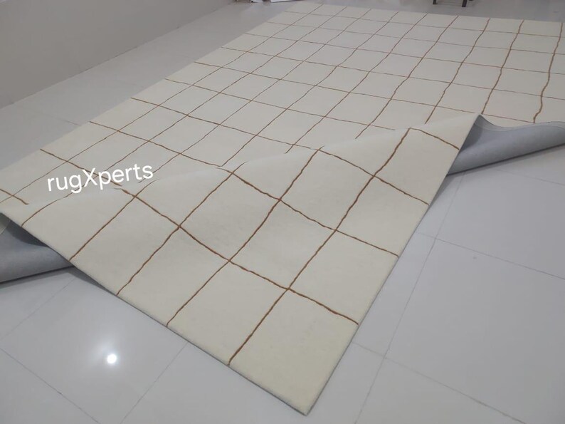 May include: A white rug with a grid pattern of brown lines. The rug is rolled up and the underside is visible.