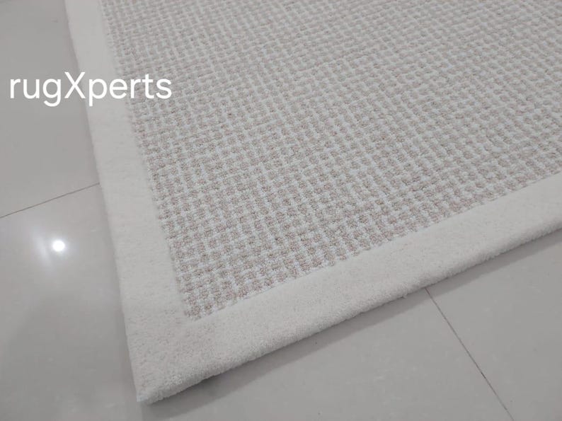 May include: Close-up of a white woven rug with a white border. The rug has a subtle texture and a slightly off-white color.