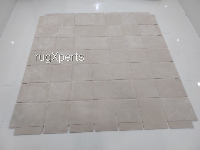 Pu&ograve; includere: Un tappeto beige fatto di quadrati singoli, con il testo "rugXperts" al centro.