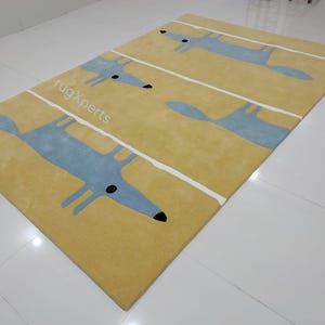 May include: A yellow rug with a white stripe pattern and blue fox silhouettes. The rug has the text "rugXperts" printed on it.