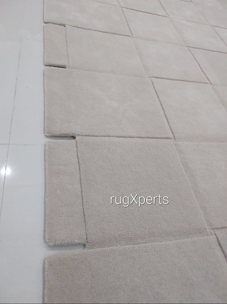 Pu&ograve; includere: Un primo piano di un tappeto beige chiaro con un motivo geometrico unico. Il tappeto &egrave; realizzato in un materiale morbido e soffice e ha una lucentezza sottile. Il tappeto &egrave; tagliato in quadrati e i bordi sono cuciti insieme per creare un design unico. Il tappeto &egrave; perfetto per aggiungere un tocco di stile moderno a qualsiasi stanza.