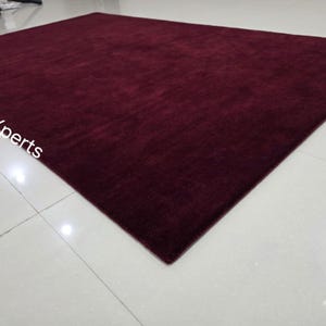 May include: A large, rectangular burgundy rug with a soft, textured surface. The rug is placed on a white tiled floor, and the overall impression is one of warmth and comfort. The rug's dimensions are not visible.