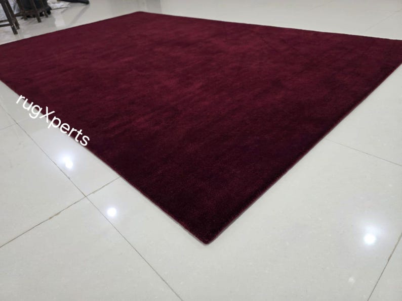 May include: A large, rectangular burgundy rug with a soft, textured surface. The rug is placed on a white tiled floor, and the overall impression is one of warmth and comfort. The rug's dimensions are not visible.
