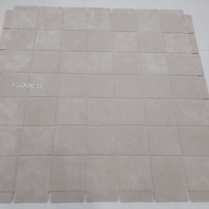 Pu&ograve; includere: Un grande tappeto quadrato di colore bianco sporco, composto da quadrati singoli cuciti insieme. Il tappeto &egrave; realizzato in un materiale morbido e soffice.