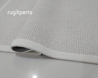 Peut inclure: Gros plan sur un tapis blanc avec un motif texturé subtil. Le tapis a une bordure blanche et est roulé, montrant le dessous.
