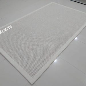 May include: White woven rug with a white border. The rug is made of a textured material and has a subtle sheen.