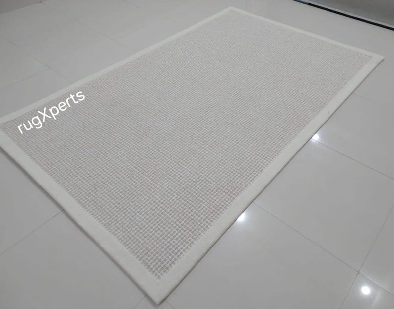May include: White woven rug with a white border. The rug is made of a textured material and has a subtle sheen.