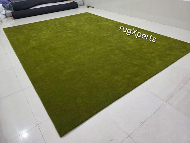 May include: A large, rectangular, olive green rug. The rug has a soft, plush texture and is displayed on a tiled floor. The text "rugXperts" is visible in the upper right corner.