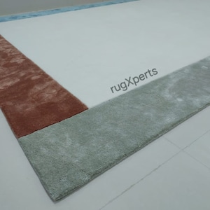 May include: A rectangular rug with a white central area and borders in shades of rust, light green, and light blue. The rug has a soft, plush texture, suitable for a living room or bedroom.