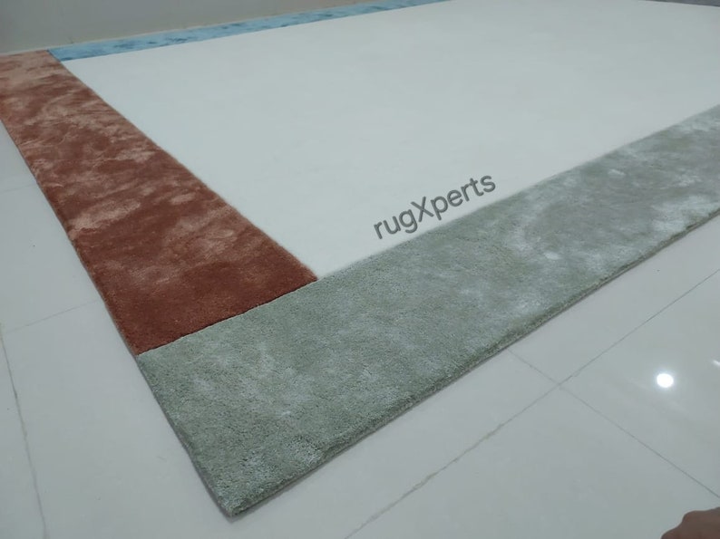 May include: A rectangular rug with a white central area and borders in shades of rust, light green, and light blue. The rug has a soft, plush texture, suitable for a living room or bedroom.