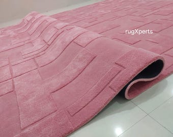 May include: A pink area rug with a geometric pattern. The rug is rolled up and the edge of the rug is visible. The rug has a black backing.