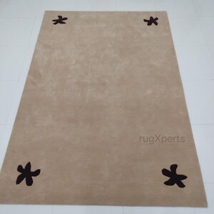 May include: A rectangular beige rug with four dark brown star-shaped designs evenly spaced on the corners. The rug has a soft, plush texture and is suitable for living rooms or bedrooms.
