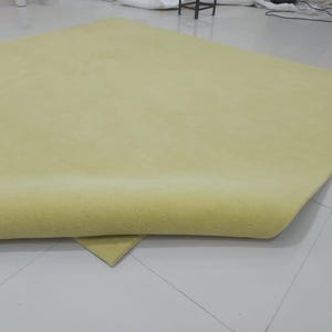 May include: A large, folded, light yellow fabric or material, possibly a rug or textile. The material is smooth and appears to be soft, with a slight sheen. The edges are neatly finished, and the overall impression is of a high-quality product.