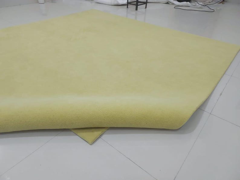May include: A large, folded, light yellow fabric or material, possibly a rug or textile. The material is smooth and appears to be soft, with a slight sheen. The edges are neatly finished, and the overall impression is of a high-quality product.