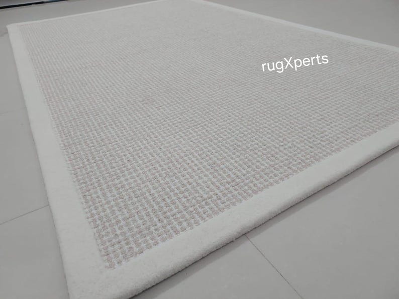 May include: A white rug with a subtle textured pattern and a white border. The rug is made of a soft, comfortable material and is perfect for adding a touch of elegance to any room.