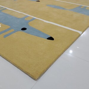May include: A yellow rug with a repeating pattern of blue stylized dogs. The rug has white stripes running across it.