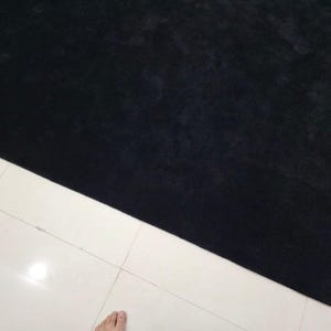 May include: A large, rectangular black rug with a soft, textured surface. The rug is positioned diagonally across white tiled flooring, creating a contrast in colour and texture. The rug's dark colour suggests a cozy and inviting atmosphere.