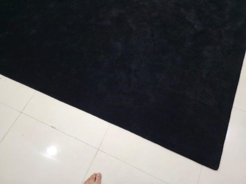 May include: A large, rectangular black rug with a soft, textured surface. The rug is positioned diagonally across white tiled flooring, creating a contrast in colour and texture. The rug's dark colour suggests a cozy and inviting atmosphere.