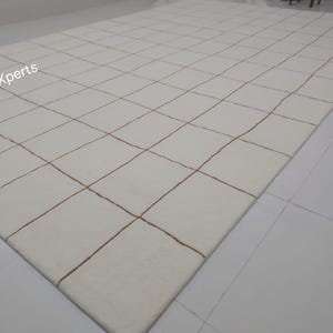 May include: White rug with a grid pattern of thin brown lines. The rug is made of a soft, plush material.