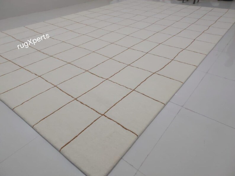 May include: White rug with a grid pattern of thin brown lines. The rug is made of a soft, plush material.