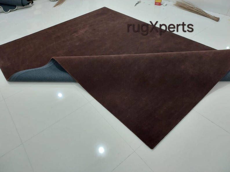 May include: A large, rectangular brown rug with a dark blue backing is partially folded over, revealing the underside. The rug is made of a soft, plush material. The image is taken from an elevated angle.