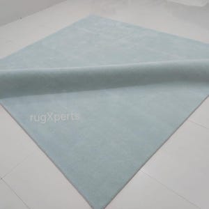 May include: A light blue rectangular rug with a rolled edge. The rug is made of a soft material and is displayed on a white tiled floor. The text "rugXperts" is visible on the rug.