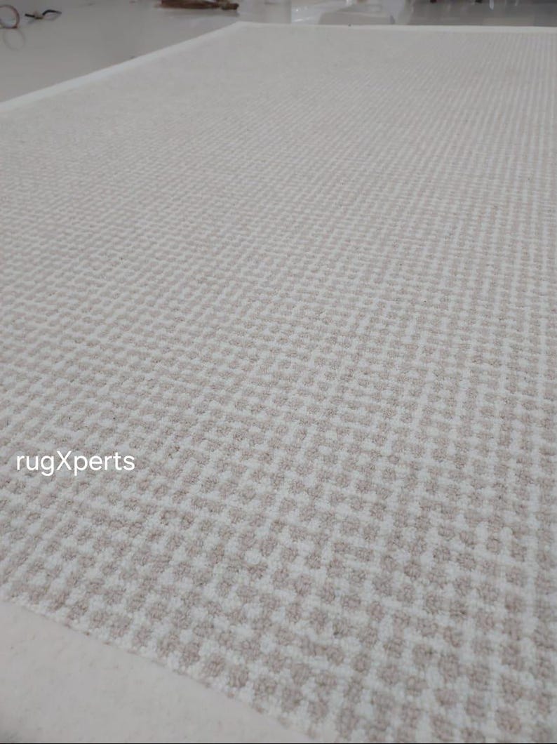 May include: A close-up of a white and beige patterned rug with a subtle geometric design. The rug has a white border and is made of a soft, textured material.