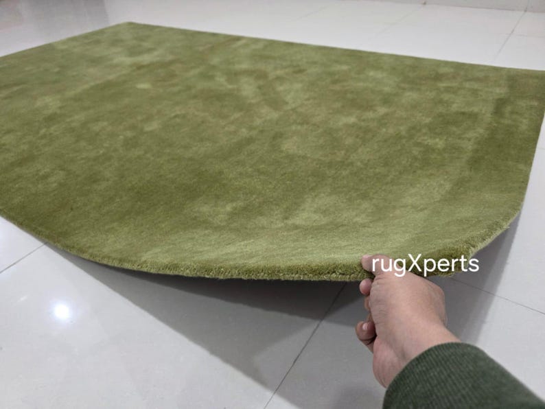 May include: A light green, semi-circular rug with a soft, textured surface. The rug is a solid colour and appears to be made of a plush material. The edge of the rug is slightly curved. The text "rugXperts" is visible.
