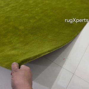 May include: A close-up shot of a bright green rug with a soft, textured pile. The edge of the rug is lifted, showing its construction. The text "rugXperts" is visible. The rug is made of a plush material, likely for comfort and warmth.
