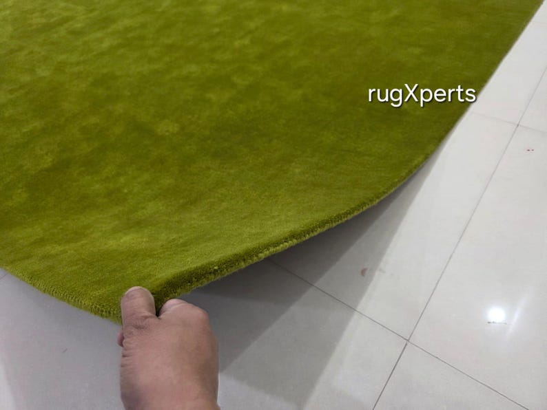 May include: A close-up shot of a bright green rug with a soft, textured pile. The edge of the rug is lifted, showing its construction. The text "rugXperts" is visible. The rug is made of a plush material, likely for comfort and warmth.